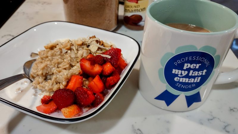 Bowl of oatmeal and berries next to a mug of coffee that shows a blue ribbon with "Professional per my last email sender" on it