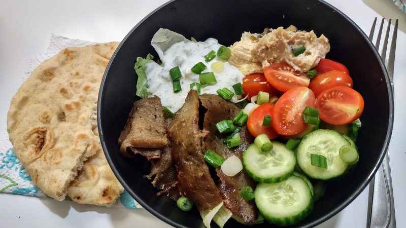 Simple Meal Planning: A gyro bowl with gyro meat, cucumbers, tomatoes, hummus, and tzatziki on a bed of lettuce, with pita bread on the side.